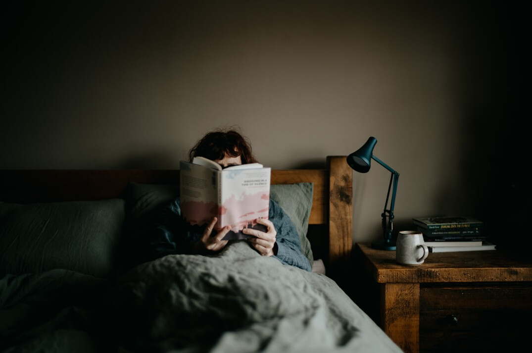 person reading book in bed at night